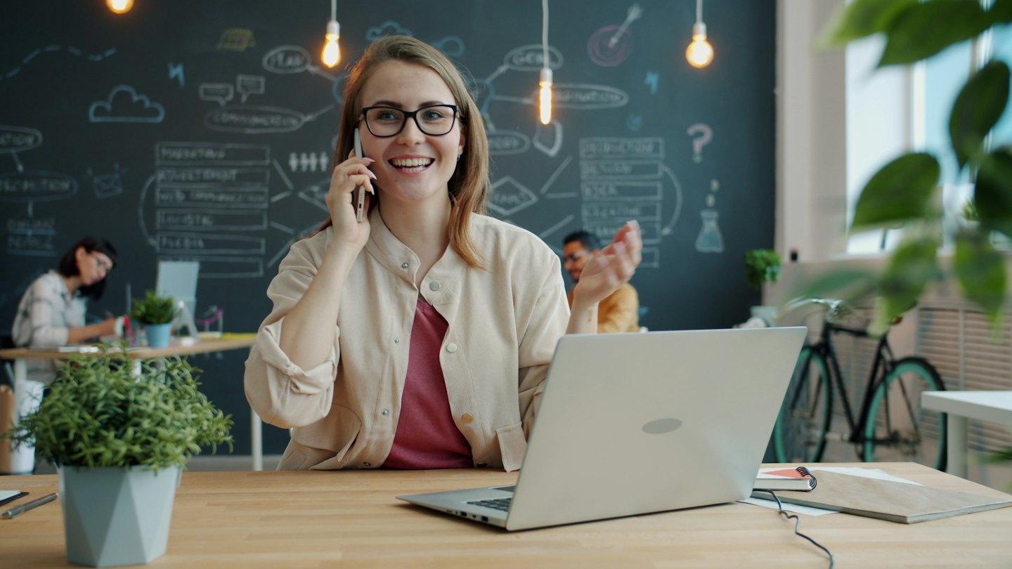 Woman with glasses talks on phone in a modern office.